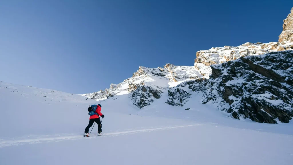 A skier is walking up the hill. Skitouring in Alps. Sunny weather. Adventure winter sport