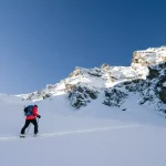 A skier is walking up the hill. Skitouring in Alps. Sunny weather. Adventure winter sport
