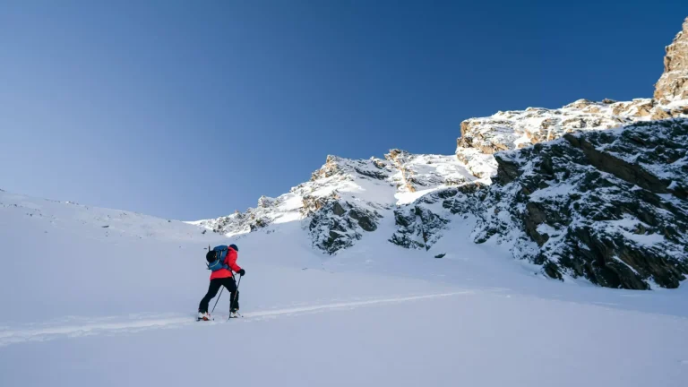 A skier is walking up the hill. Skitouring in Alps. Sunny weather. Adventure winter sport